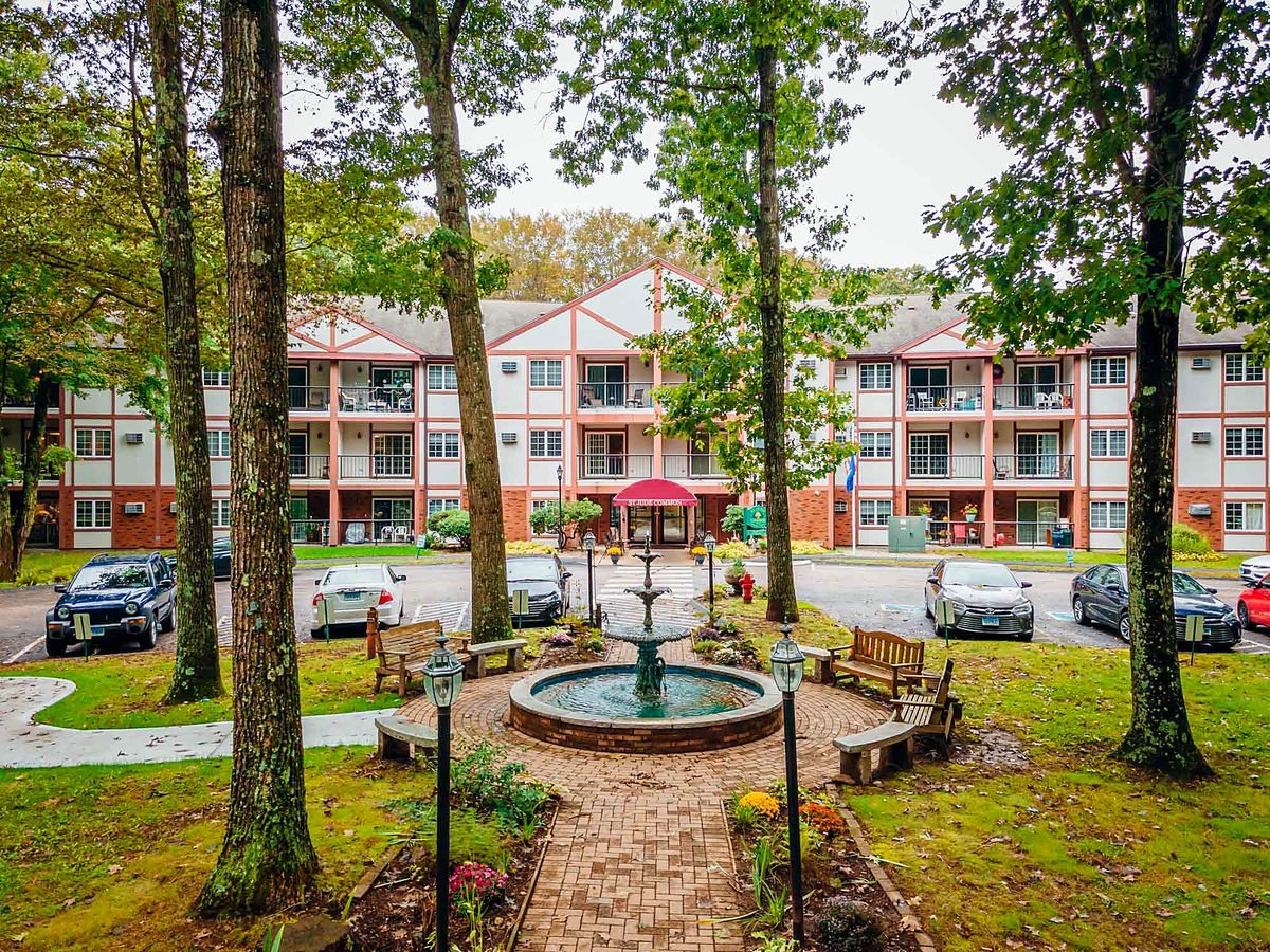 St. Jude Common in Norwich, CT — three-storey residence with coral and white timbered facade above a brick fountain courtyard